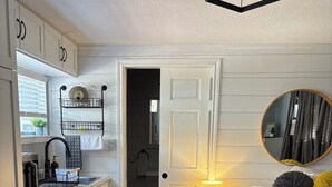 Ein Schlafzimmer mit Bett, Nachttisch und Spiegel. Es gibt eine Küchenzeile mit Schränken und Spüle.
