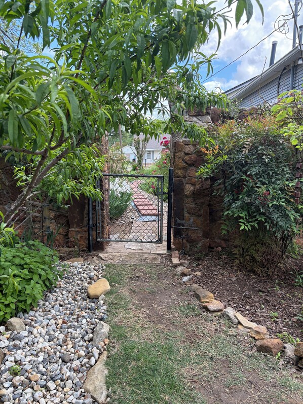 Un sentier de jardin menant à une entrée fermée par un portail, entouré de verdure et d’un mur de pierres.