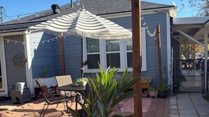 Ein Haus mit überdachter Terrasse, Gartenmöbeln und Pflanzen in Töpfen.