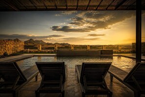 Un espace piscine avec des chaises longues et une vue sur les montagnes au coucher du soleil.