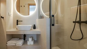 Ein modernes Badezimmer mit rundem Spiegel, weißem Waschbecken und einer Duschkabine.