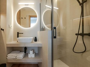 Un baño moderno con un espejo redondo, un lavabo blanco y una ducha con mampara de vidrio.
