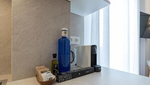 Eine moderne Küche mit Arbeitsplatte, einer Kaffeemaschine, einem Wasserkocher, einer Olivenölflasche und einer Kapselbox.