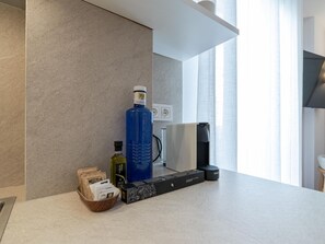 Una cocina moderna con una encimera, una cafetera, un hervidor, una botella de aceite de oliva y una caja de cápsulas de café.