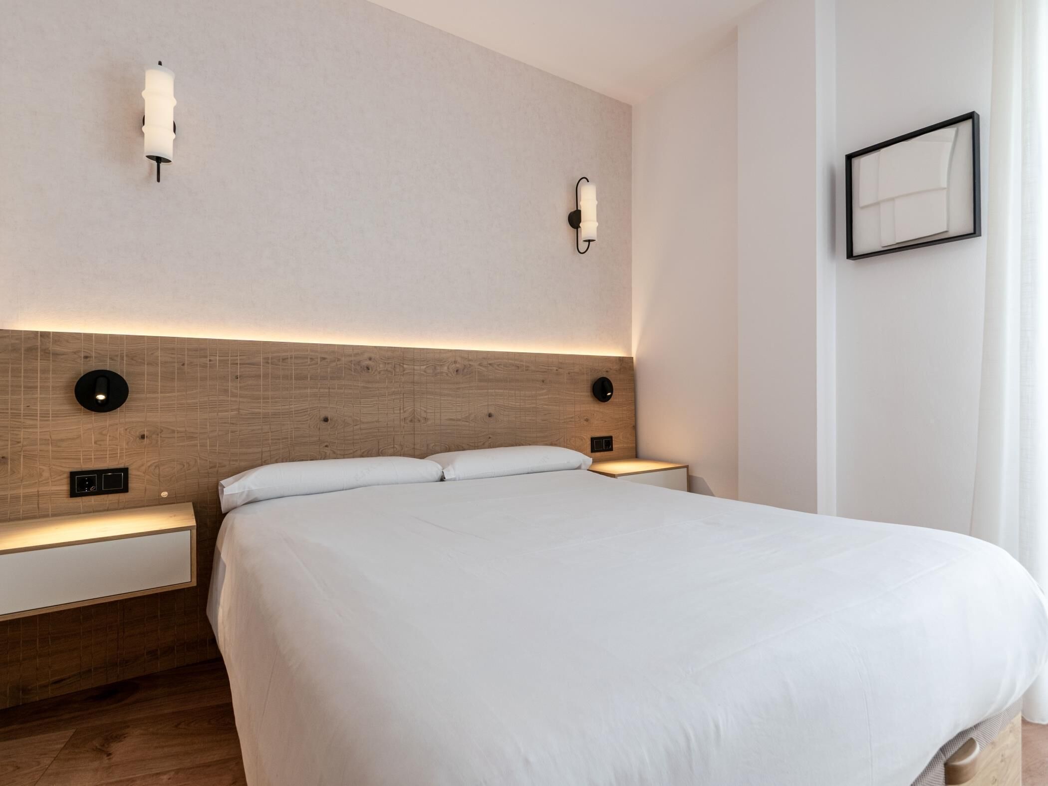 Een moderne hotelkamer met een groot bed, een houten hoofdeinde, nachtkastjes en wandlampen.