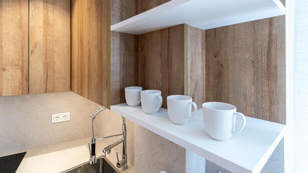 Eine moderne Küche mit Holzvertäfelung, einem Edelstahl-Spülbecken und weißen Regalen mit Tassen.
