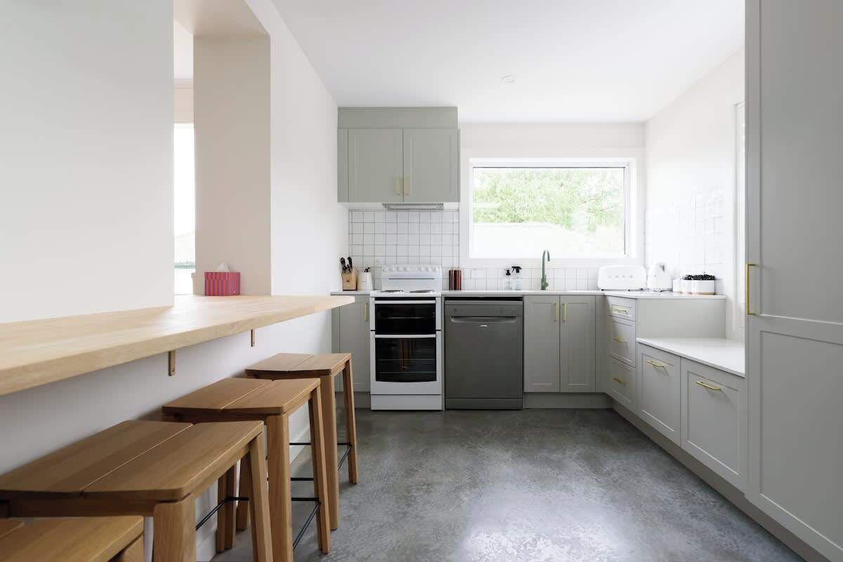 A modern kitchen with white cabinets, a wooden countertop, and a window providing natural light.