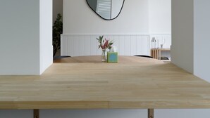 Ett minimalistiskt rum med ett träbord, en rund spegel och en liten växt.