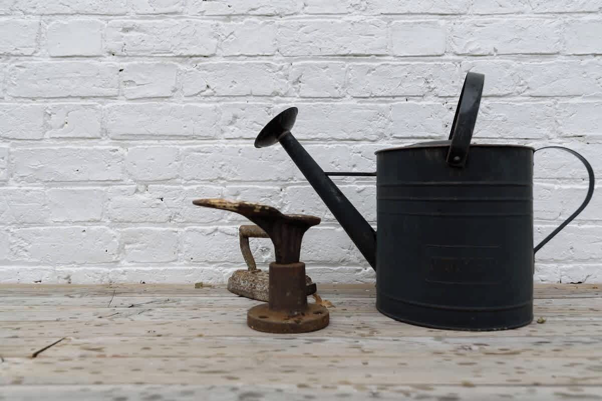A rustic metal watering can and a metal bucket against a white brick wall.