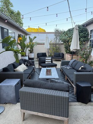 An outdoor patio with wicker furniture, a table with a glass top, and string lights. - Bohome Reserve: Culver City Studios 3 bedroom Cozy City Space (Culver City)