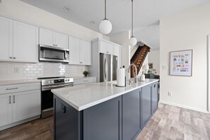 A modern kitchen with white cabinetry, stainless steel appliances, a marble countertop, and pendant lighting. - Walk to Mass Ave: HOT TUB, private yard, parking (Indianapolis)