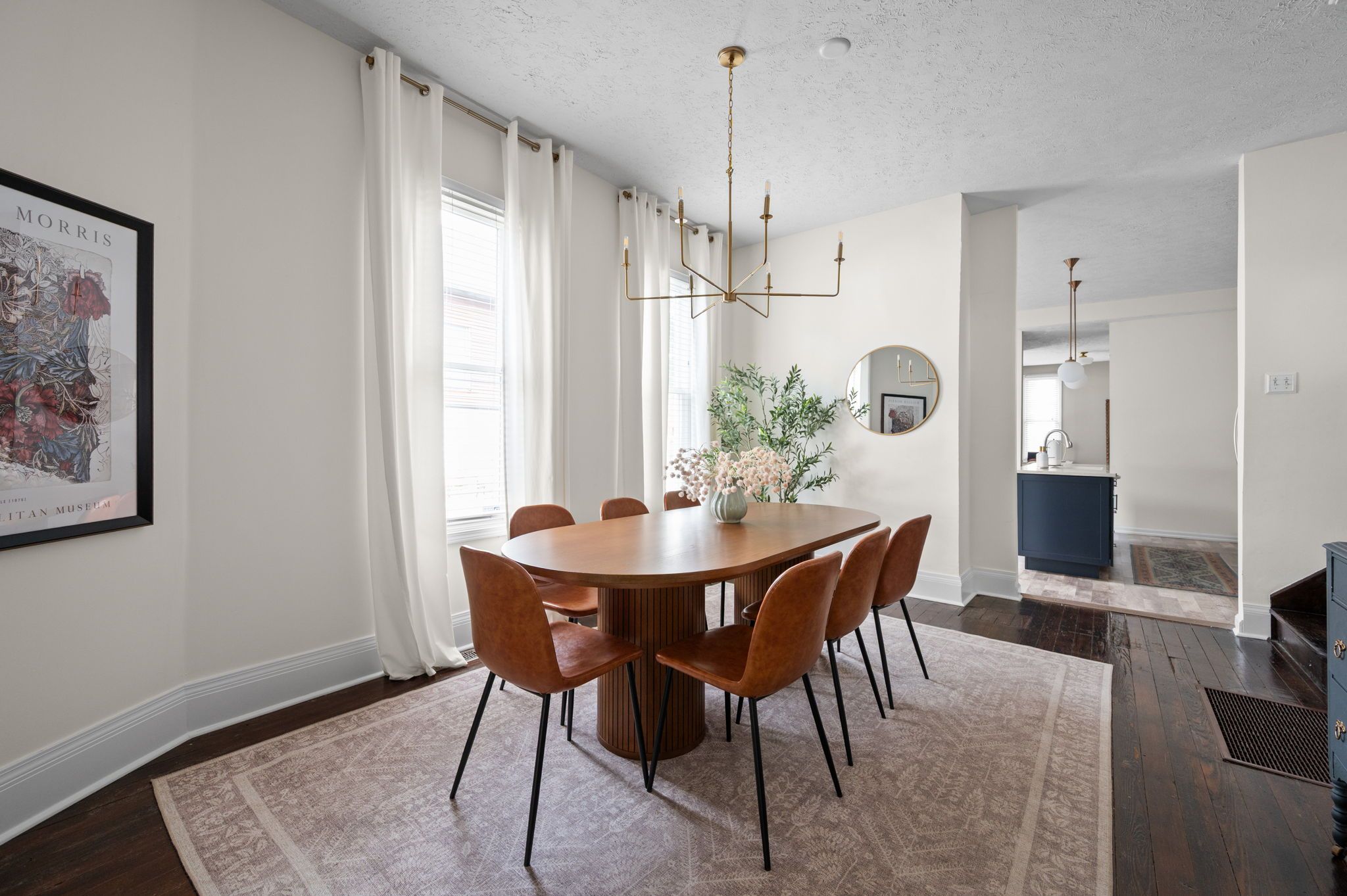 A dining area with a round table, six chairs, a chandelier, and a large mirror on the wall.