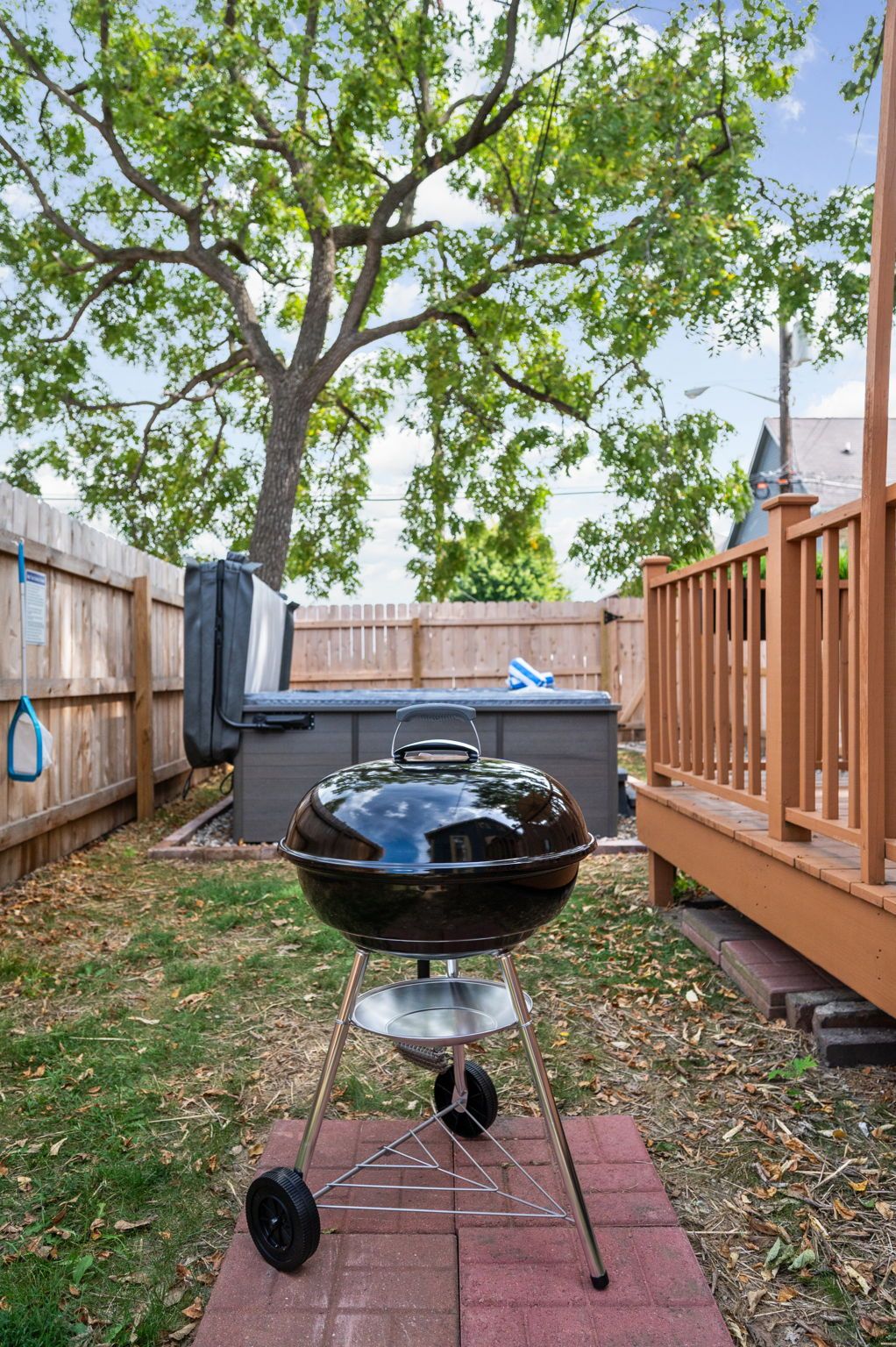 A barbecue grill in a backyard with a wooden fence, a tree, and a grill cover.
