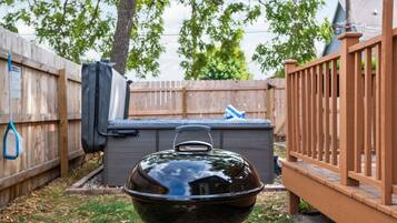 A barbecue grill in a backyard with a wooden fence, a tree, and a grill cover.