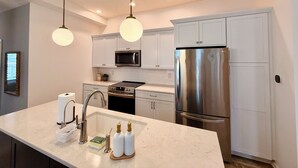 A modern kitchen with white cabinetry, stainless steel appliances, a marble countertop, and pendant lighting. - Hot tub - Mass Ave - Sleeps 9 - Free parking (Indianapolis)