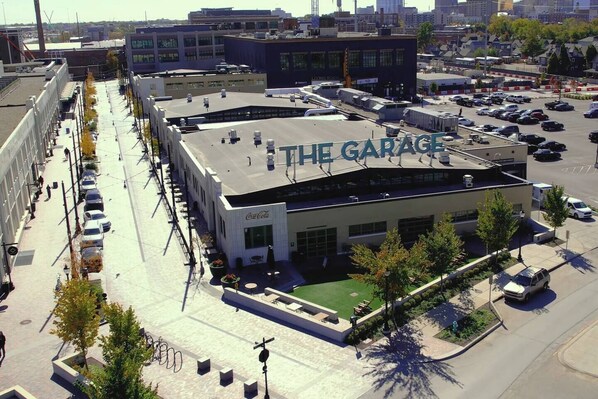 A building with a sign reading 'THE GARAGE' on the roof, surrounded by a parking lot and adjacent buildings.