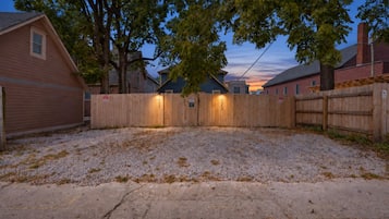 A gravel driveway leading to a wooden fence with numbered gates, surrounded by residential buildings.