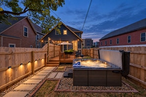 A backyard with a hot tub, wooden deck, and a house.