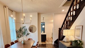 A dining area with a wooden table and chairs, a chandelier, and a staircase leading to an upper level. - Hot tub - Mass Ave - Sleeps 9 - Free parking (Indianapolis)