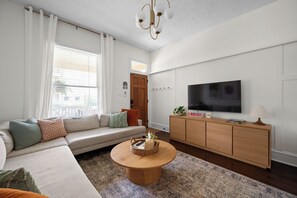 A modern living room with a sofa, a coffee table, a TV, and a wooden cabinet. - Walk to Mass Ave: HOT TUB, private yard, parking (Indianapolis)