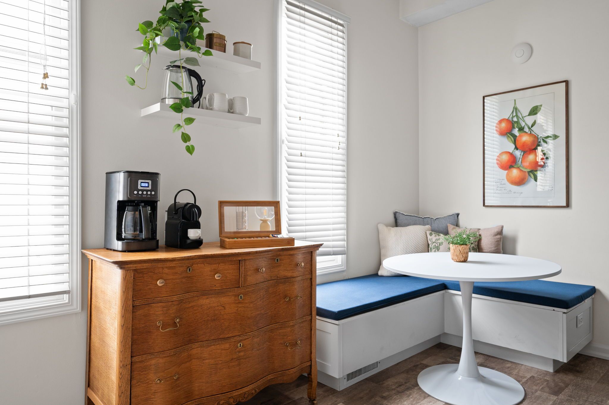 A corner seating area with a wooden dresser, a coffee maker, and a framed picture on the wall.