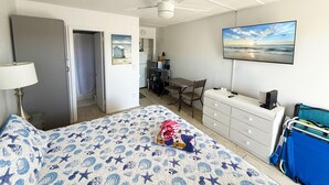 A hotel room with a bed, a desk, a chair, a TV, and a ceiling fan. - Venice Villas Upper Floor - Beachside (Venice)