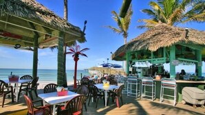 A beachside restaurant with thatched-roof structures, outdoor seating, and a view of the ocean. - Venice Villas Upper Floor - Beachside (Venice)