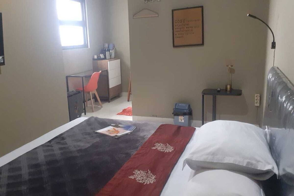 Una habitación de hotel con una cama, un escritorio, una silla, una mesita, un televisor montado en la pared y un cartel enmarcado.