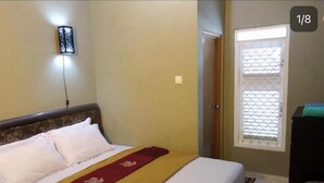 Ein Hotelzimmer mit einem Bett, einem Nachttisch, einem Fenster mit Jalousien und einer wandmontierten Leuchte.