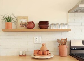 Een keuken met een witte bakstenen achterwand, een houten plank met keramiek, een grill en een potplant.