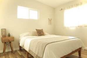 A bedroom with a bed, a nightstand, a window, and a wall-mounted macrame piece.