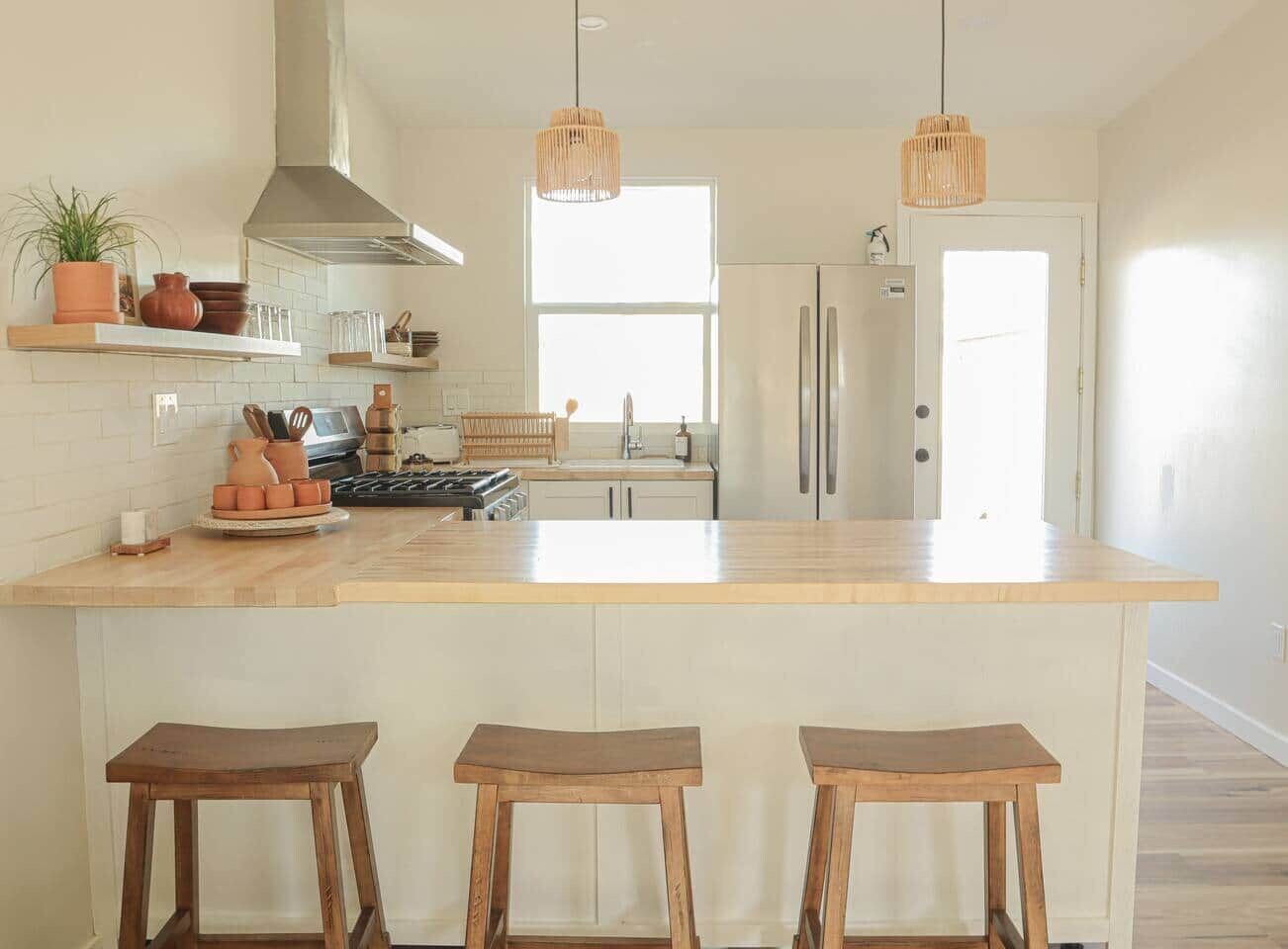 A modern kitchen with a central island, bar stools, pendant lighting, and a view to the dining area.