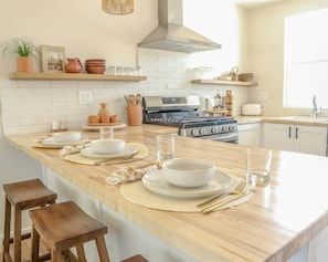 A kitchen with a central island, wooden stools, and a variety of kitchenware.