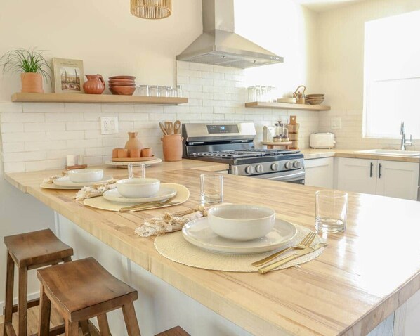 A kitchen with a central island, wooden stools, and a variety of kitchenware.