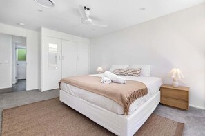 Ein modernes Schlafzimmer mit einem großen Bett, einem Deckenventilator und einem Nachttisch mit Lampe.