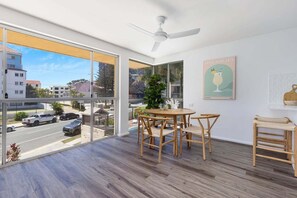Ein modernes Zimmer mit großem Fenster, Deckenventilator, Esstisch mit Stühlen und einer Topfpflanze.