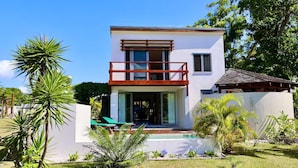 Ein zweistöckiges Haus mit Balkon, umgeben von tropischen Pflanzen und einem Pool.
