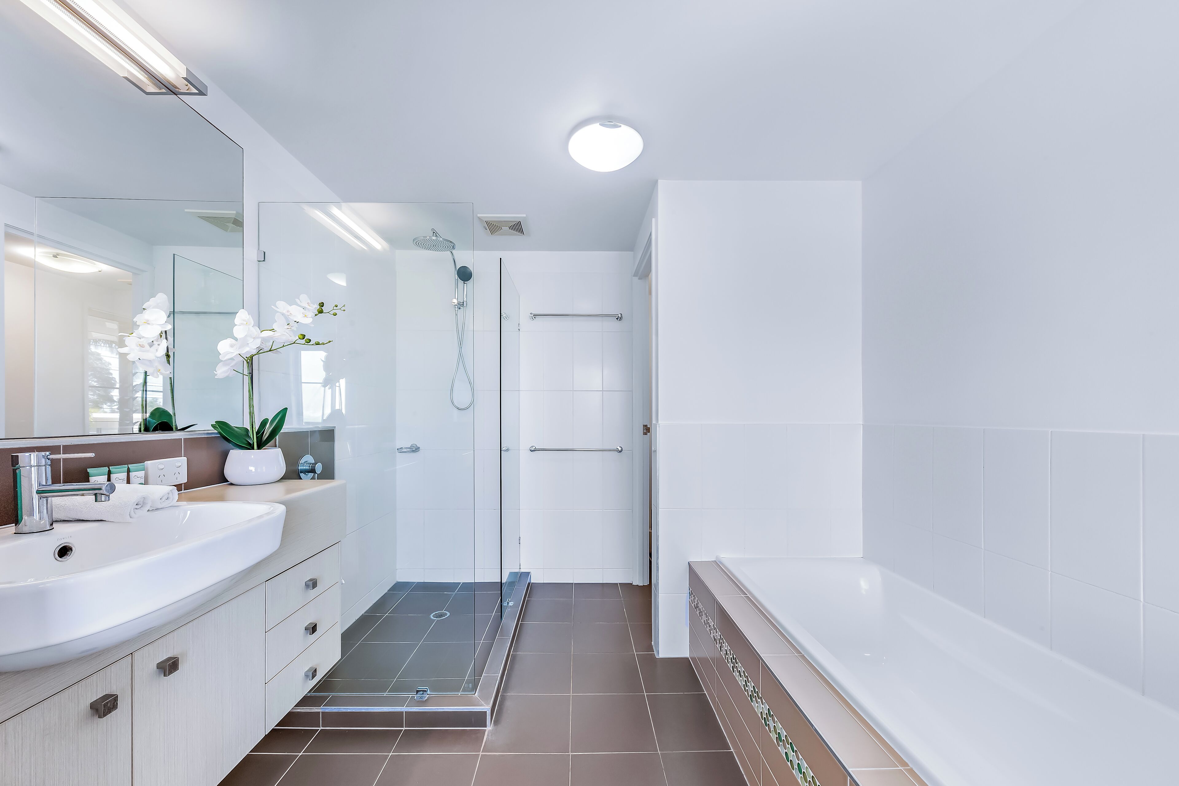 Een moderne badkamer met een douchecabine van glas, een witte wastafel en een grote spiegel.
