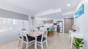 Una cocina moderna con armarios blancos, un refrigerador de acero inoxidable y una zona de comedor con mesa y sillas de madera.