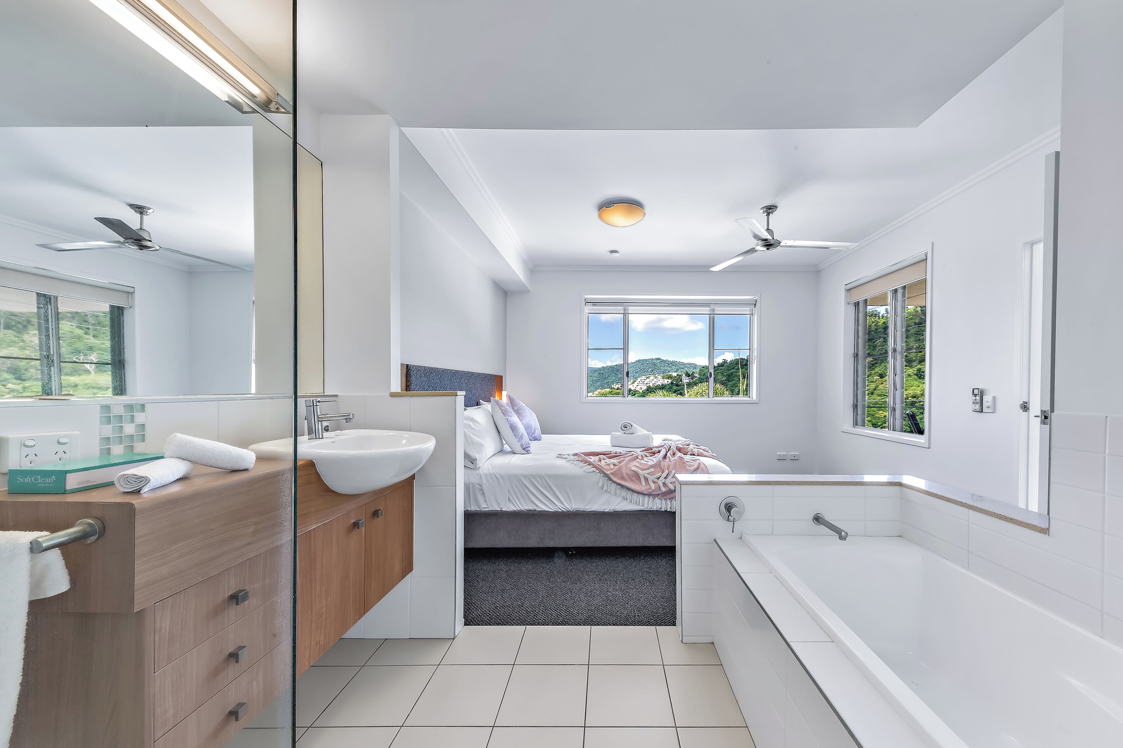 A modern bathroom with a bathtub, a large mirror, and a window with a view of greenery.