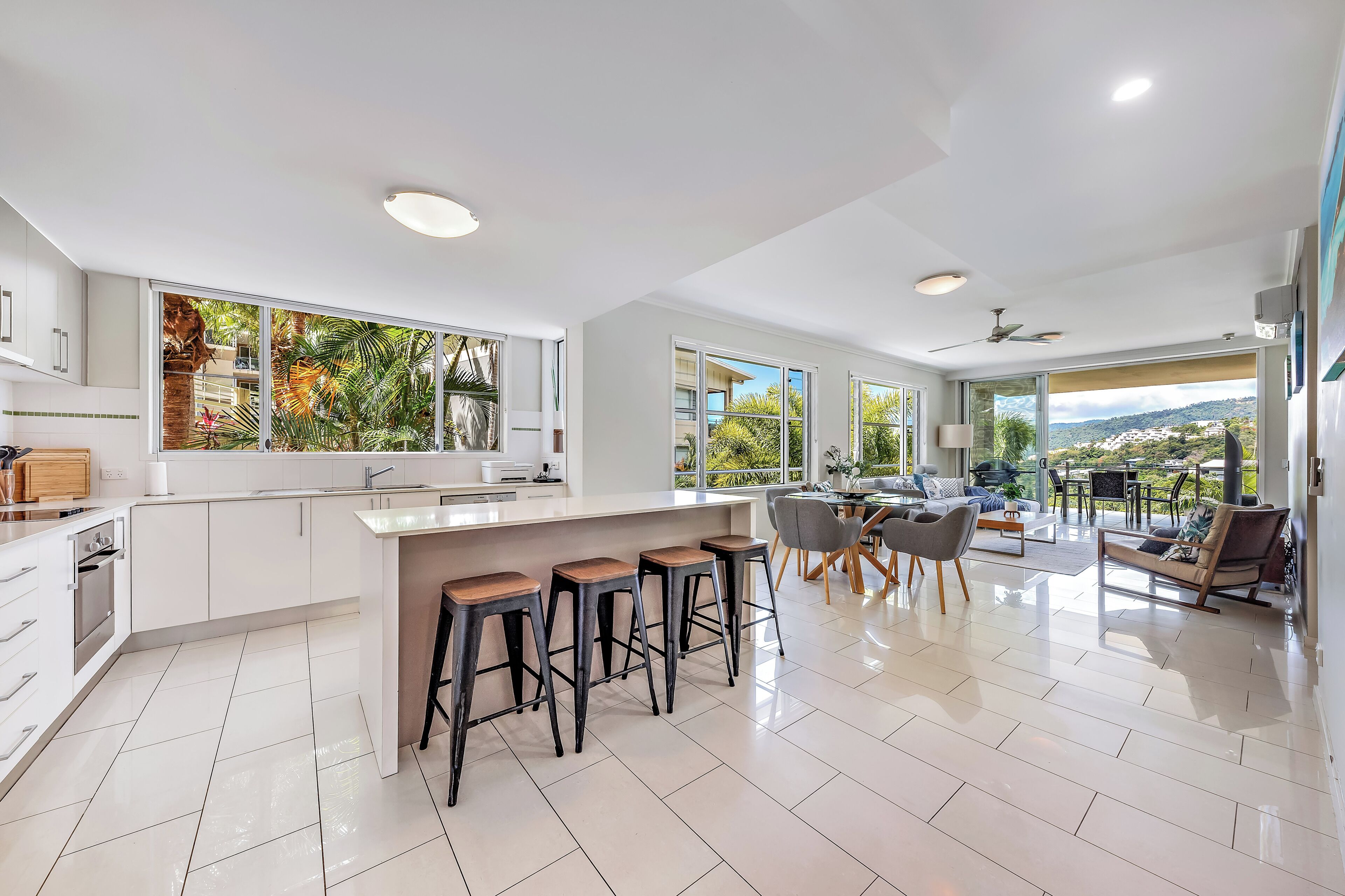 A modern kitchen with a large island, bar stools, and a dining area with a view.