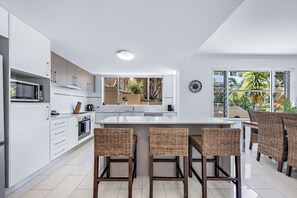 Una cocina moderna con armarios blancos, electrodomésticos de acero inoxidable y una isla central con taburetes de bar.
