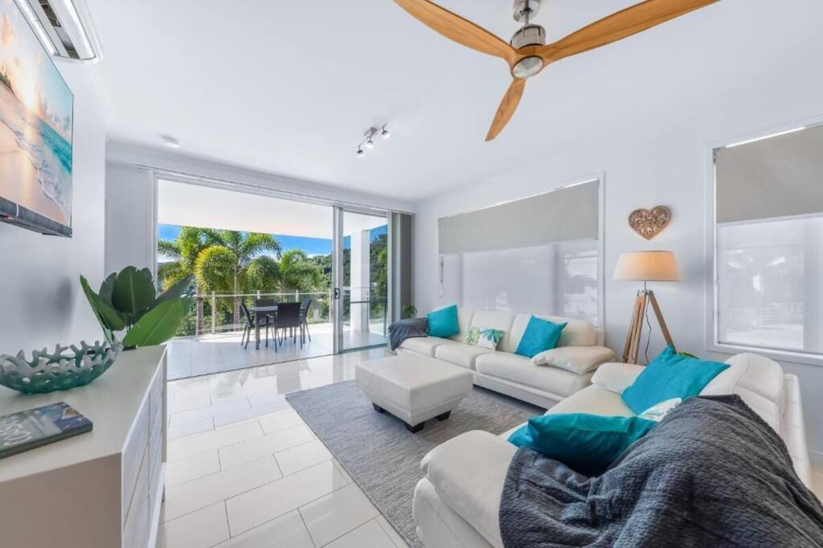 Una sala de estar moderna con un sofá blanco, un ventilador de techo y vistas al exterior.