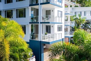 Un hotel de varios pisos con balcones, mobiliario exterior y abundante vegetación.
