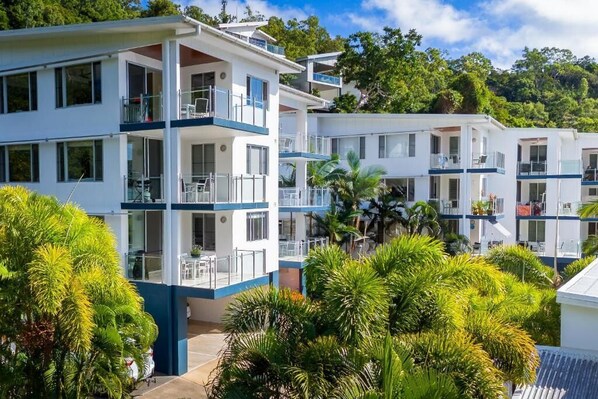 Un hotel moderno de varios pisos con balcones, rodeado de abundante vegetación.