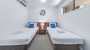 A hotel room with two single beds, a nightstand, a lamp, a wall-mounted air conditioner, and a ceiling light. - Summit Apartments Airlie Beach (Airlie Beach)