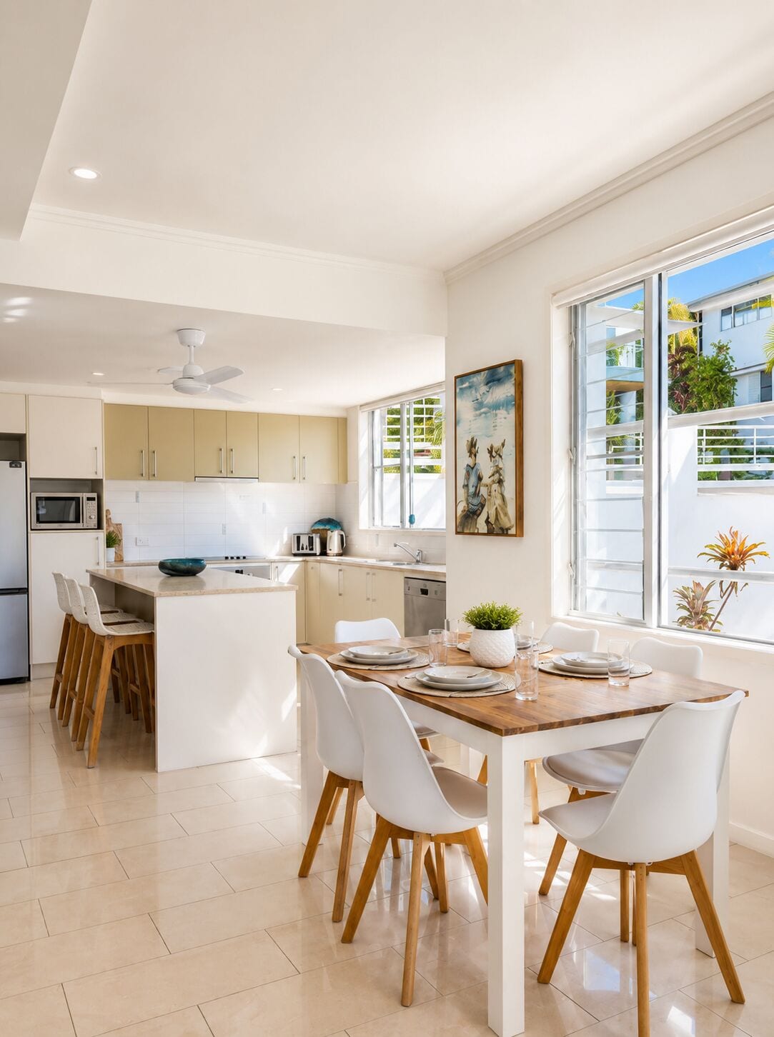 A modern kitchen with white cabinets, a central island, and a dining area with white chairs and a wooden table.