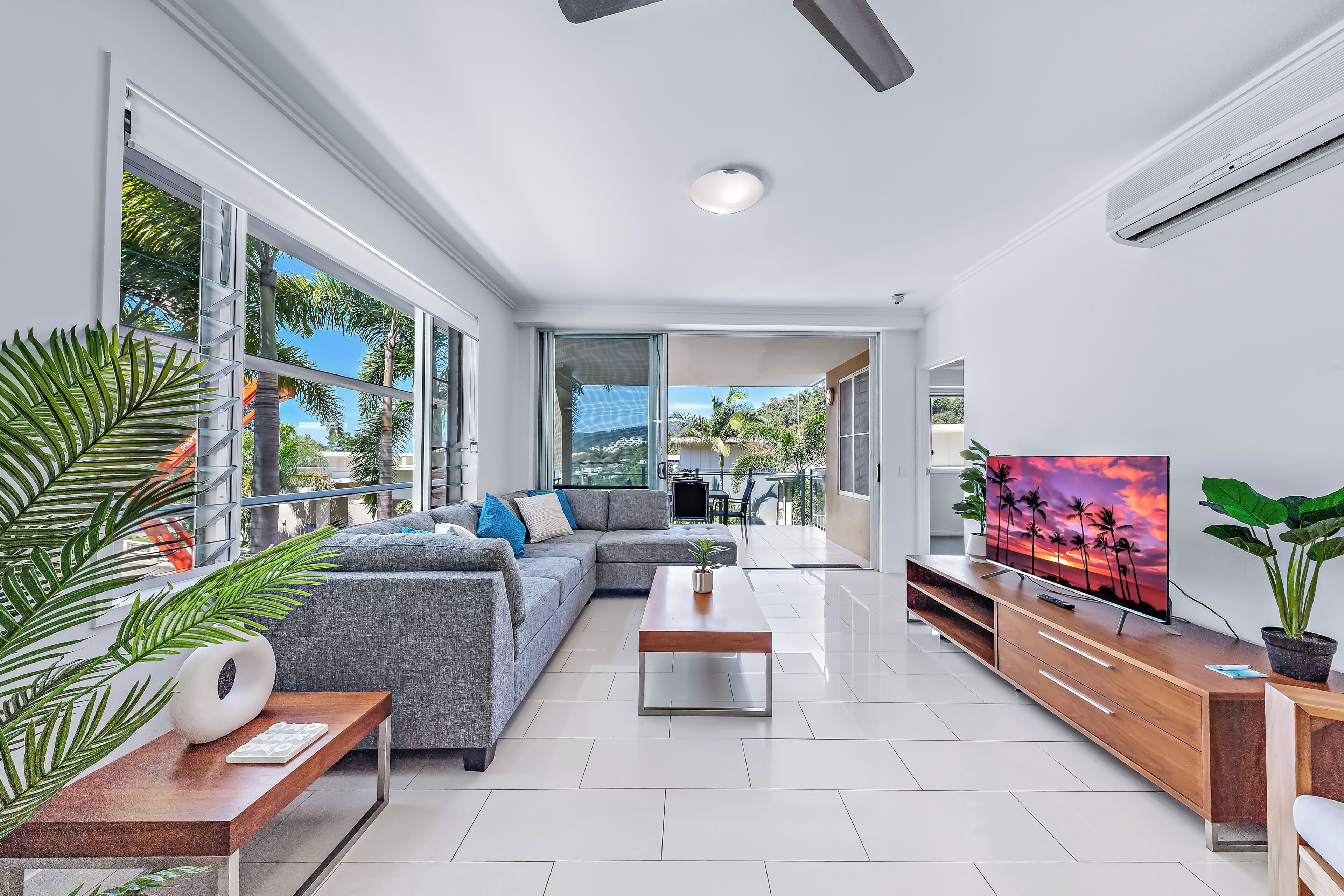 A modern living room with a sectional sofa, a coffee table, and a TV displaying a sunset scene.