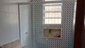 A bathroom with a toilet, a sink, a shower enclosure, and a window. - Beach House (Praia Grande)