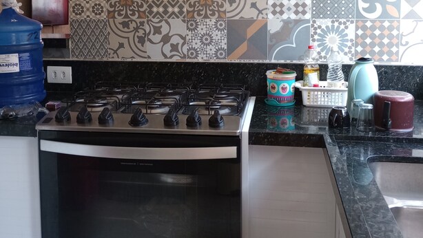 A kitchen with a gas stove, a microwave, and a variety of patterned tiles on the backsplash. - Beach House (Praia Grande)